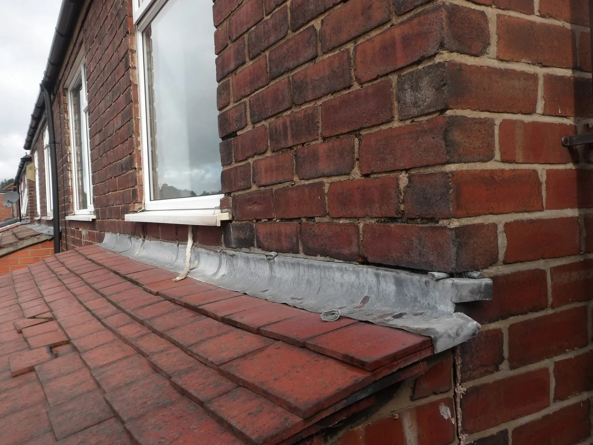 An open mortar joint at the corner of a lead-flashed roof-to-wall junction.