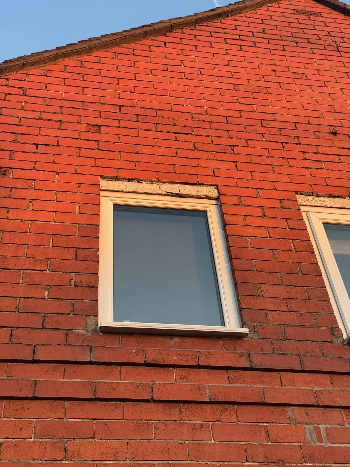 A crack through a concrete lintel above a white-framed window in a brick wall.