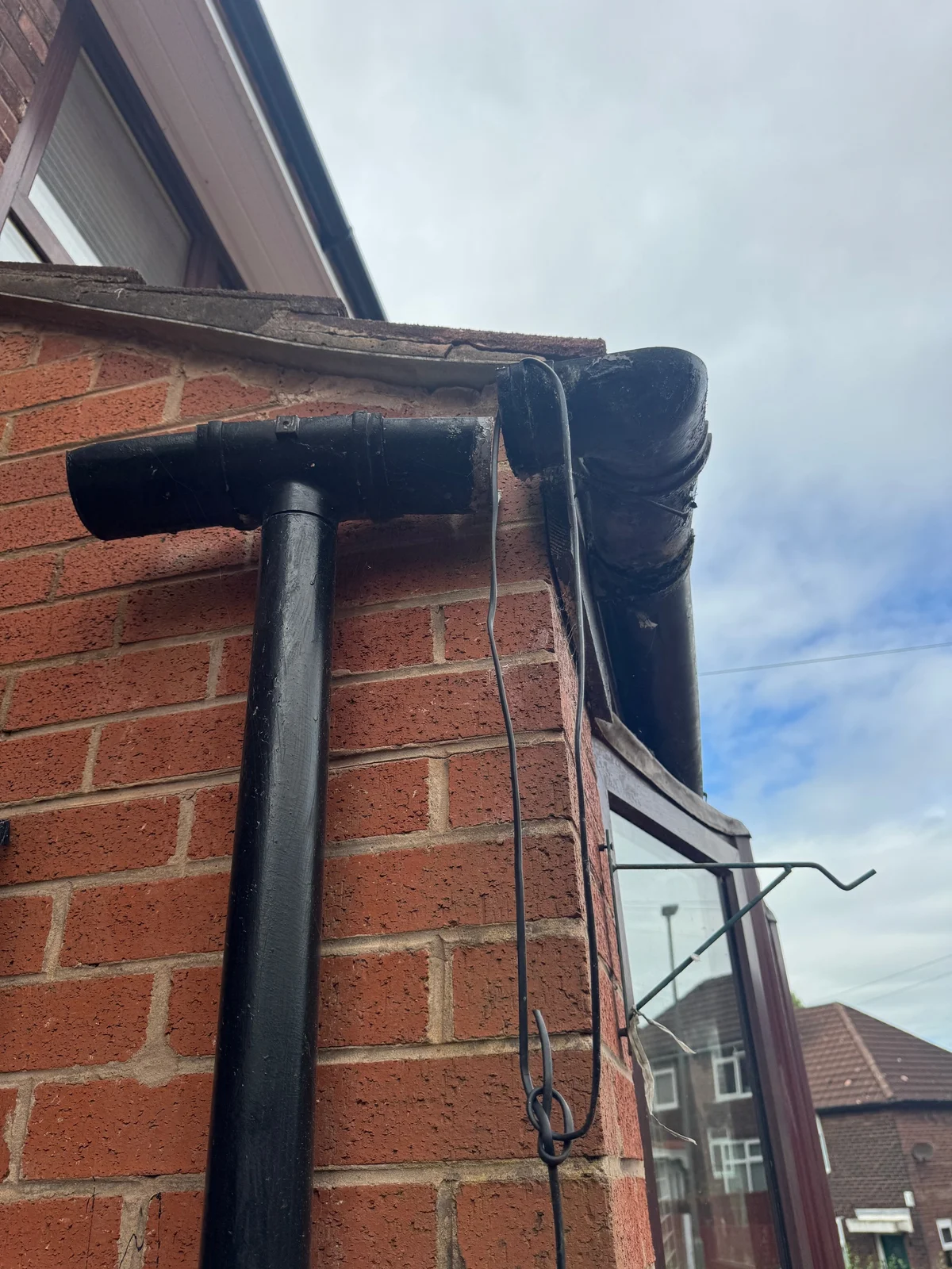 An open gap between a gutter outlet section and the corner gutter, with the downpipe still attached.
