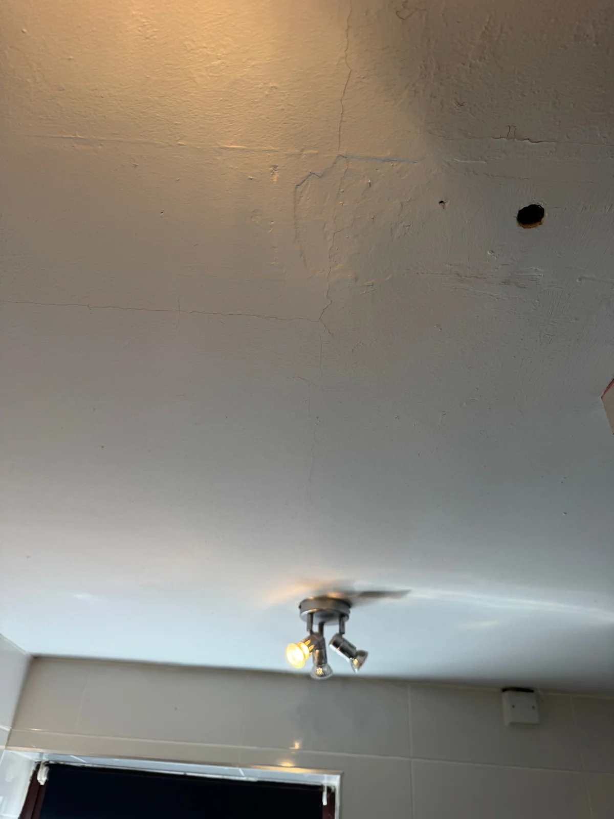 Cracking and local flaking in the painted finish of an internal ceiling.