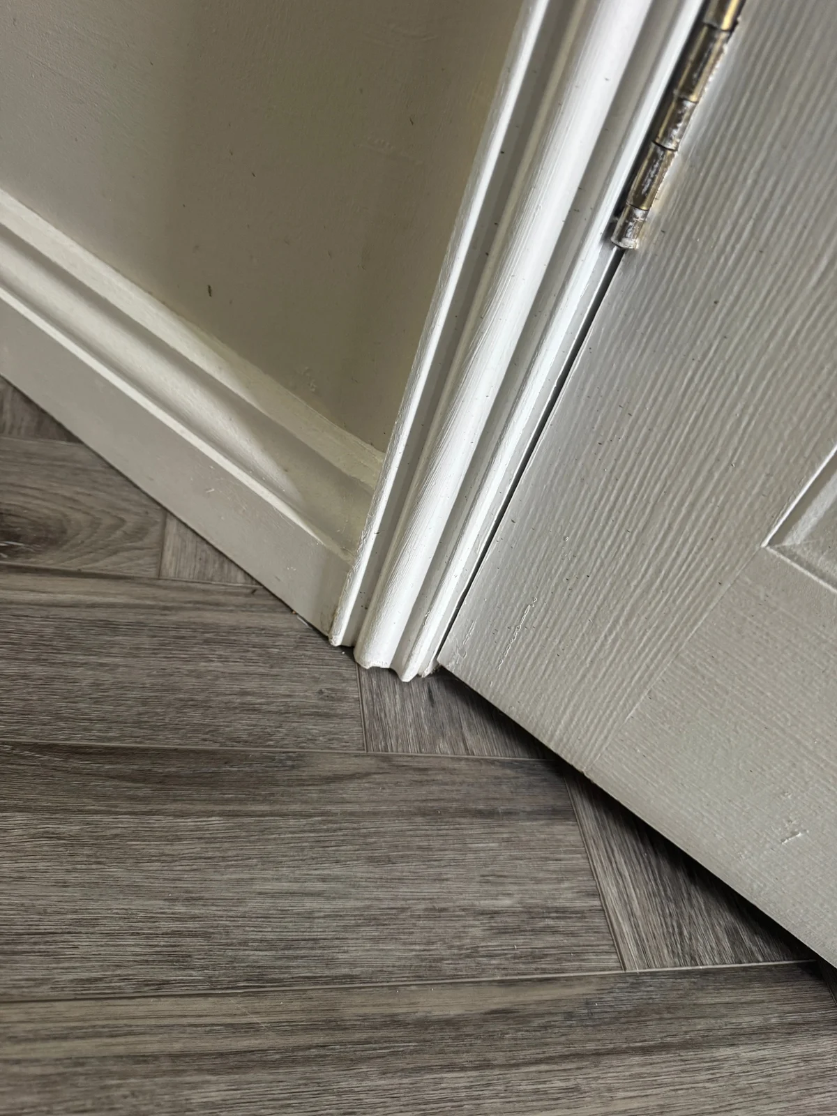 Painted skirting meets moulded door architrave above a timber-effect patterned floor.