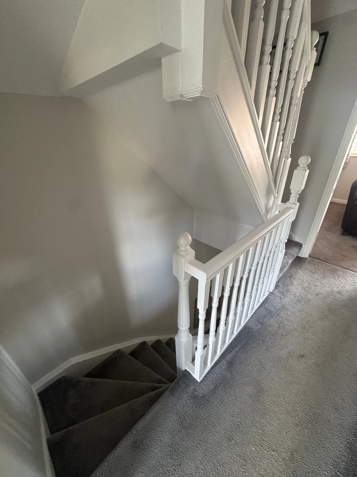 White painted newel posts and turned spindles border a carpeted landing and turning stair.