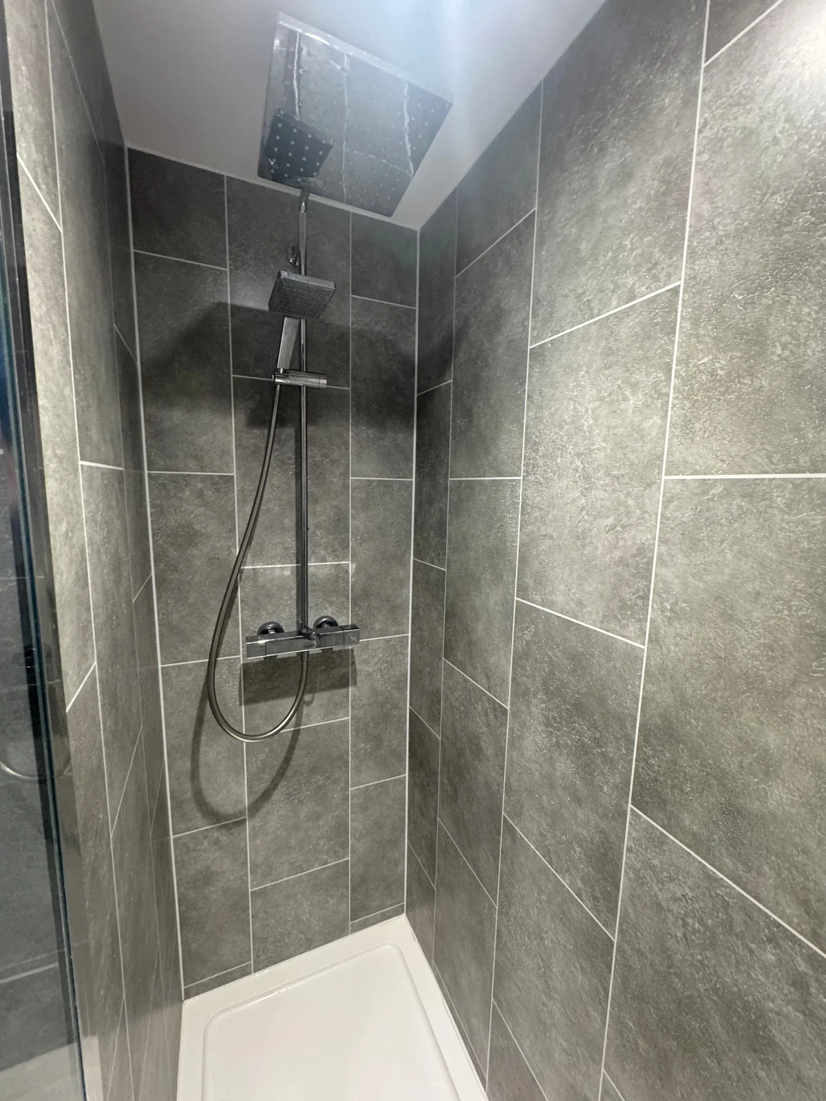 Grey rectangular wall tiles meet a white shower tray beneath a mixer shower and glass screen.