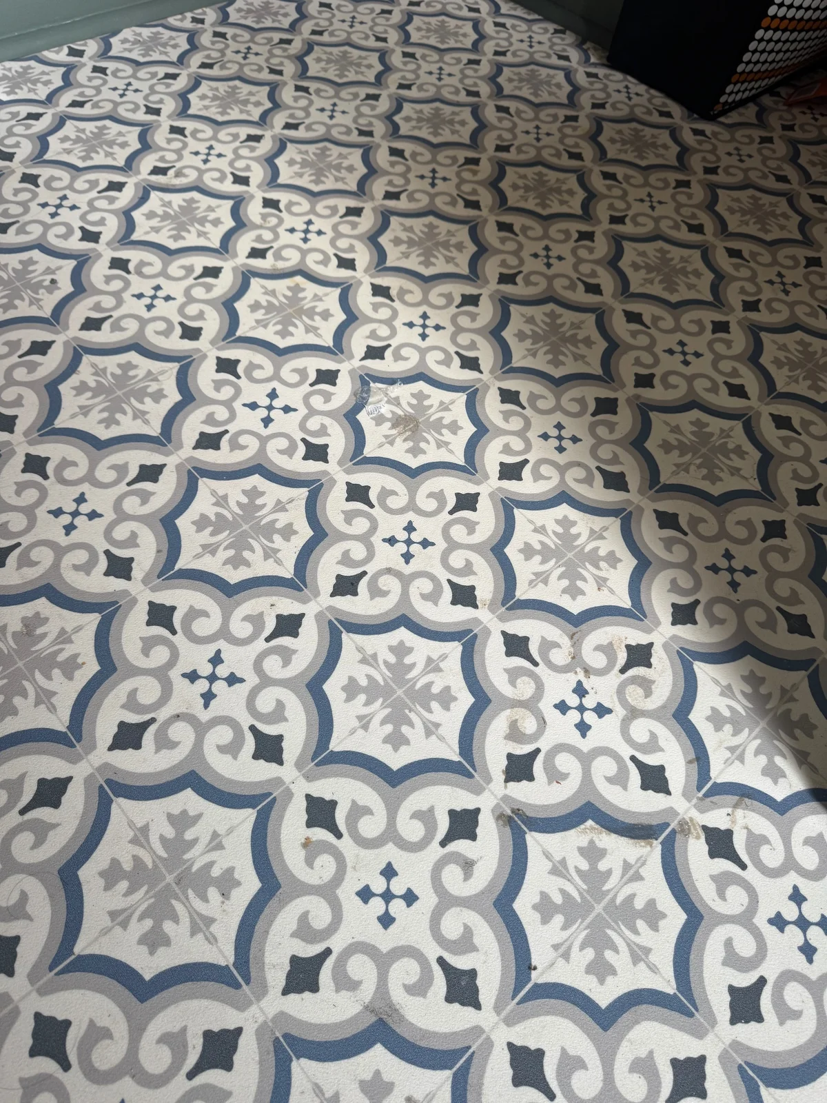 A blue, grey and cream geometric floor covering with tile-like printed divisions and local surface marks.