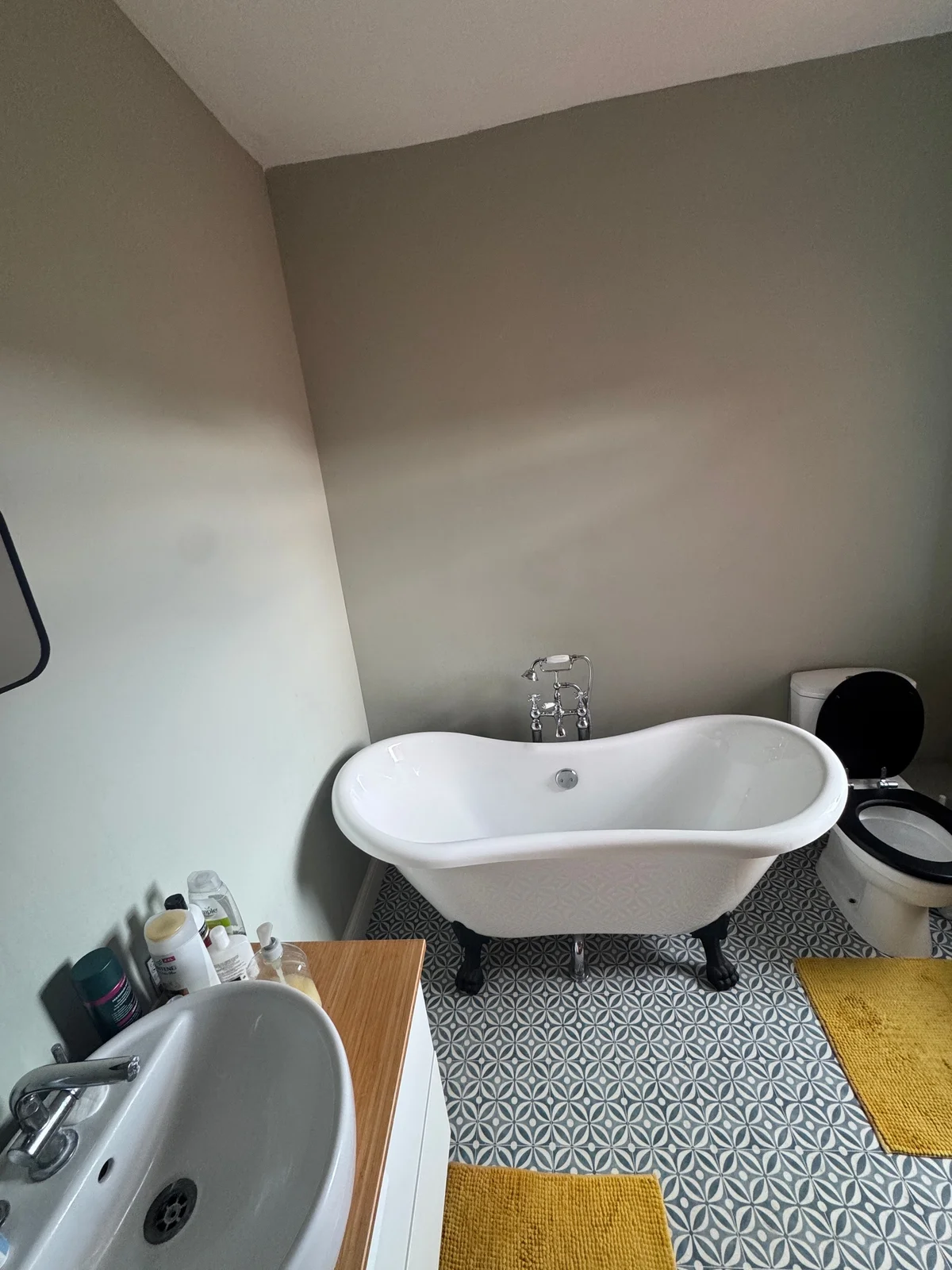 A white freestanding bath on dark feet, with taps behind and a patterned floor beneath.