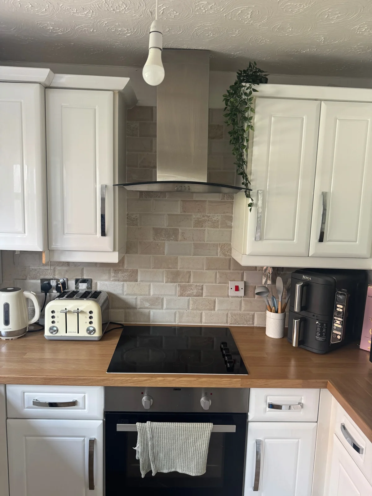 White moulded kitchen fronts around a dark hob, wood-effect worktop, tiled splashback and extractor hood.