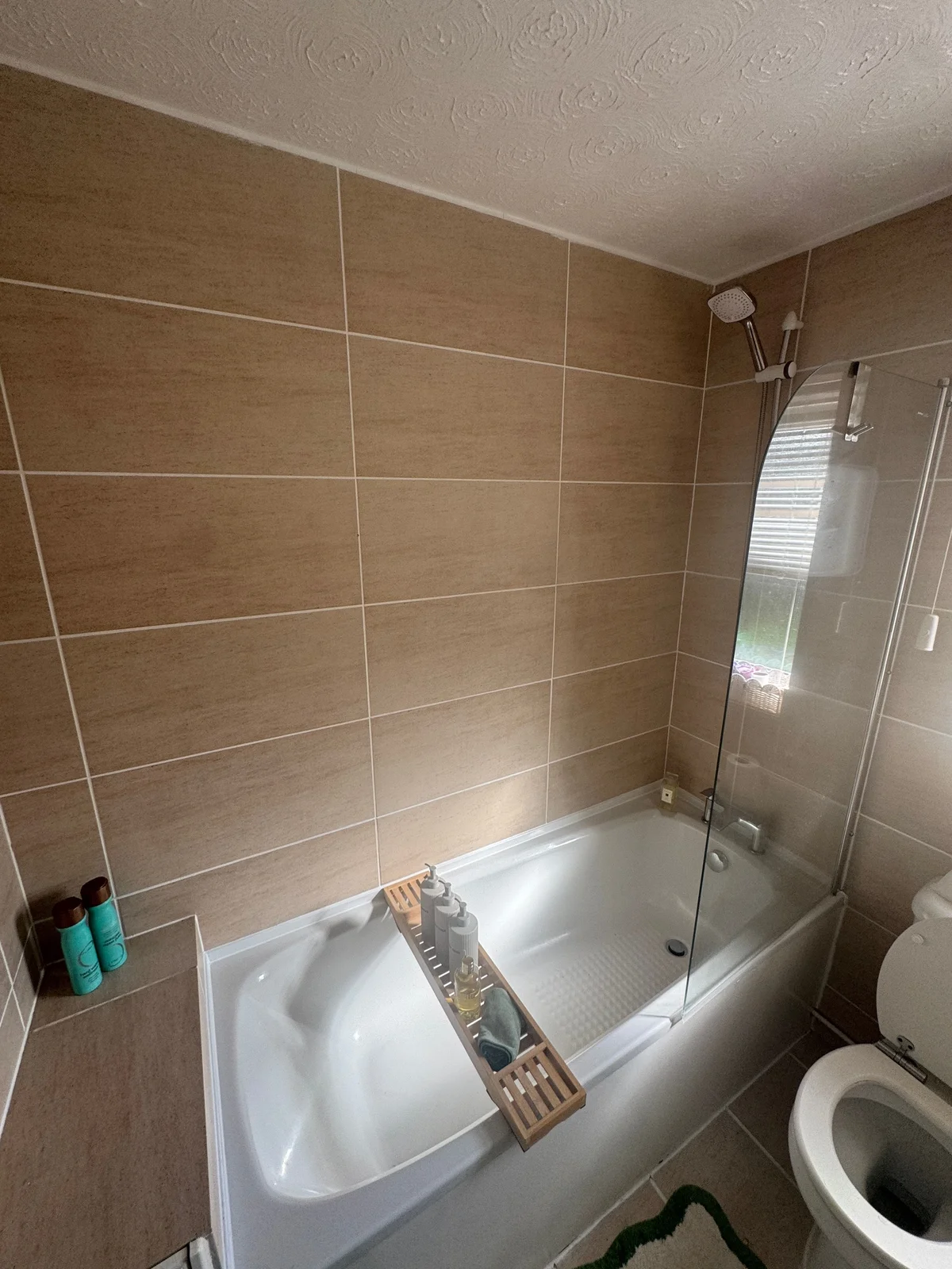 A clear glass bath screen beside an over-bath shower, tiled walls and a white bath.