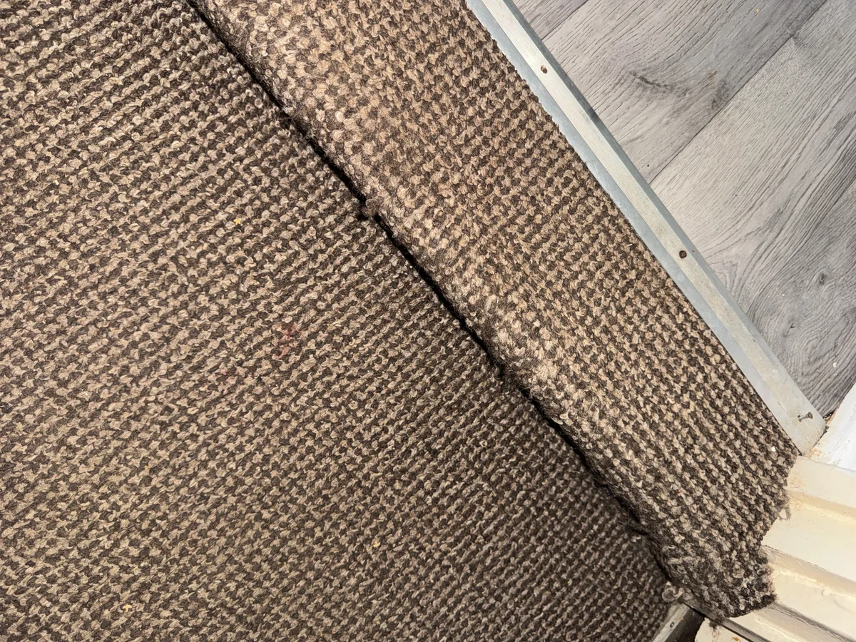 An open join in patterned carpet near a metal threshold strip and timber-effect flooring.