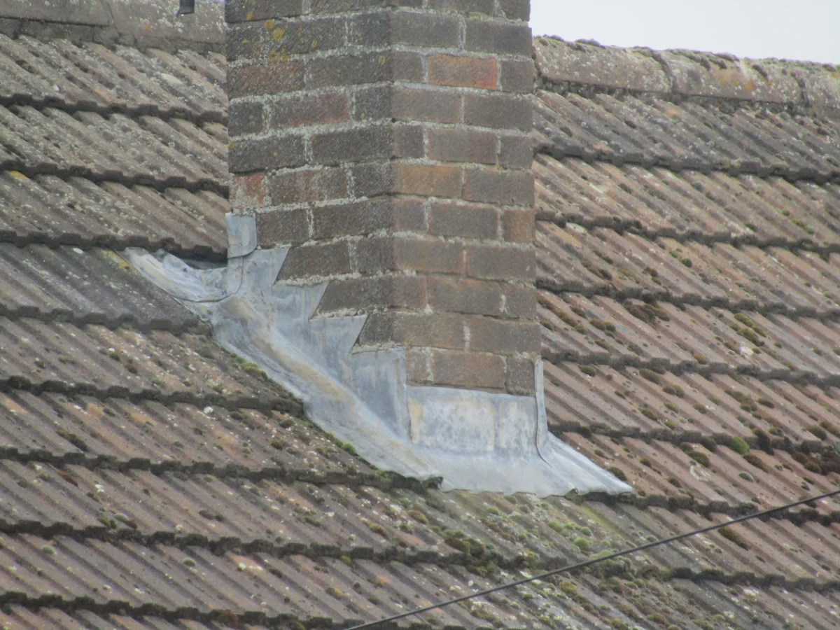Stepped lead flashing follows the side of a brick chimney, with an apron over the roof covering at its lower front, in Trimingham, Norfolk.